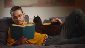 Cat lies on young man reclining in bed reading a book during pandemic - Powered by Shutterstock - Get 15% off with code: PIKWIZARD15