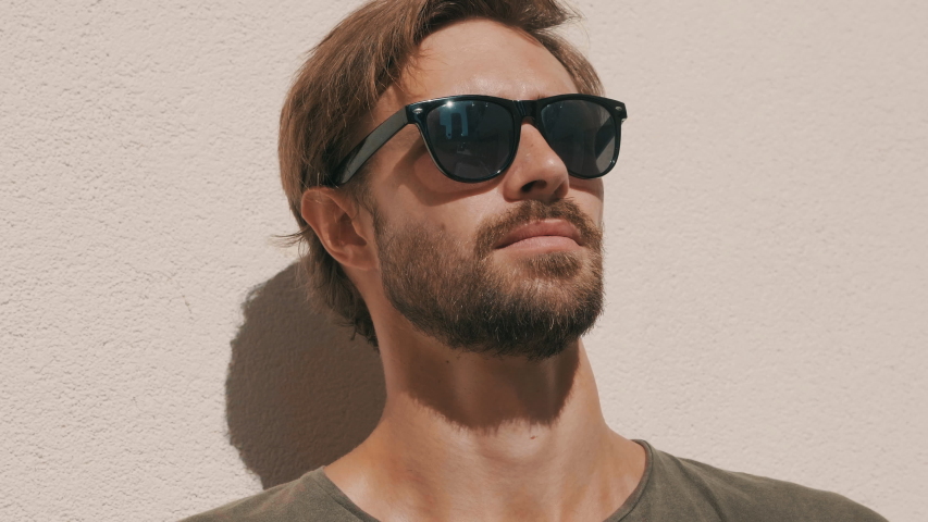 Portrait of handsome confident stylish hipster lambersexual model. Man dressed in T-shirt. Fashion male posing in the street near white wall outdoors in sunglasses