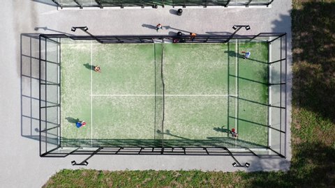 Four fit healthy young people playing paddle tennis at a green outside outdoors paddle court tennis balls hitting racket sport being sweaty fitness activity from above playing together as team friends