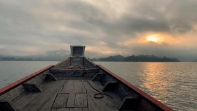Head of wooden Long tail Thai boat with mountains and sunrise in the background on Chew Lan Dam or Ratchaprapa Dam at Khao Sok National Park in Surat Thani Province, Thailand