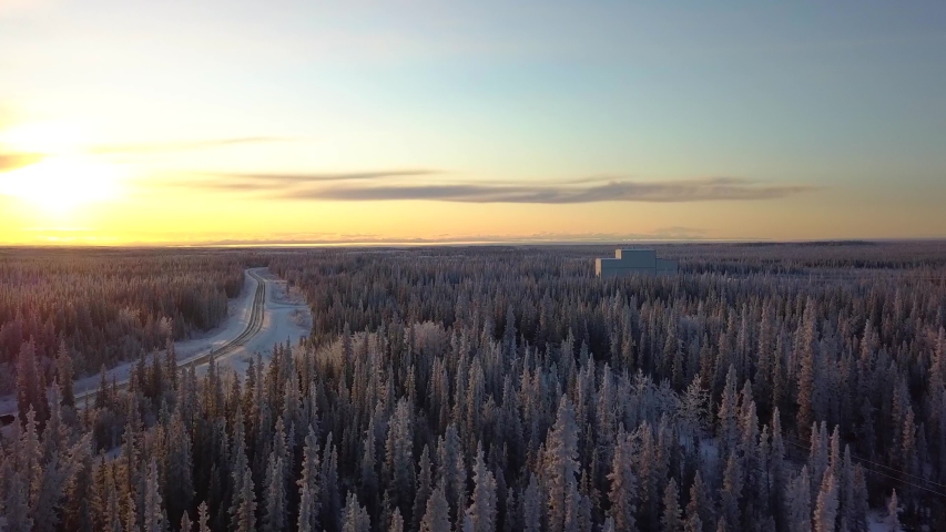 Aerial, tracking, drone shot, overlooking a car on a frozen road, in middle of Boreal forest, at sunset, on a sunny, winter evening, in Gakona, Alaska, USA