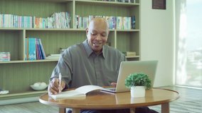 Smiling business senior old elderly Black American man, African person working from home on table with computer notebook laptop in quarantine in corona virus pandemic concept.