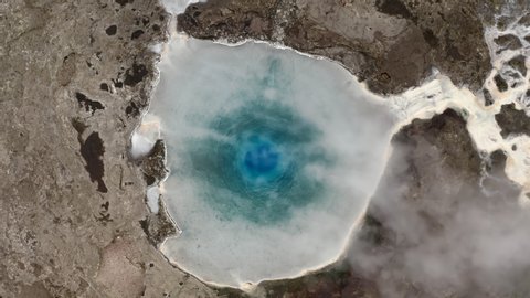 Close up aerial top down flight on geyser inside, Iceland, 4k. acid turquoise hot water inside smokes and prepares for release and white salt streaks at the stones