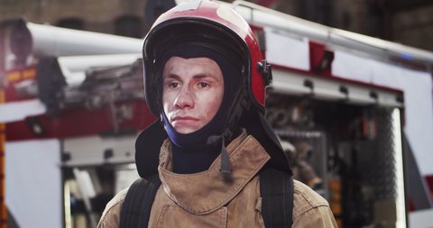 Portrait of caucasian handsome fireman in helmet and gull equipment standing next to the car and looking into camera. The concept of saving lives, heroic profession, fire safety