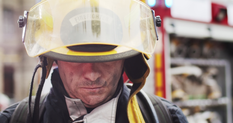 Close up portrait of strong serious fireman in helmet and gull equipment standing next to car with flashing lights on and looking into camera. Concept of saving lives, heroic profession, fire safety Royalty-Free Stock Footage #1057927882