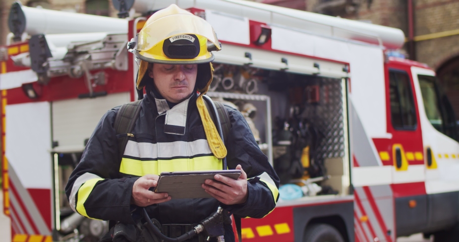 Portrait of fireman in helmet and gull equipment viewing on sides and writting data to tablet. Rescuer working with latest technologies. The concept of saving lives, heroic profession, fire safety