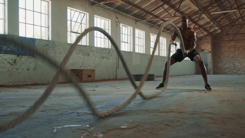 Fitness man exercising with battle rope in cross training gym inside old warehosue. Muscular man working out at empty warehouse.
 | Shutterstock HD Video #1057928533