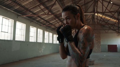 Fit young female practicing shadowboxing in old empty warehouse. Muscular build woman working out in cross training workout space

