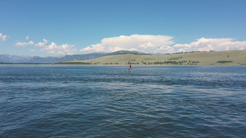 View of lake with people on paddle board in the distance and a watercraft moving across the water pulling person on board.