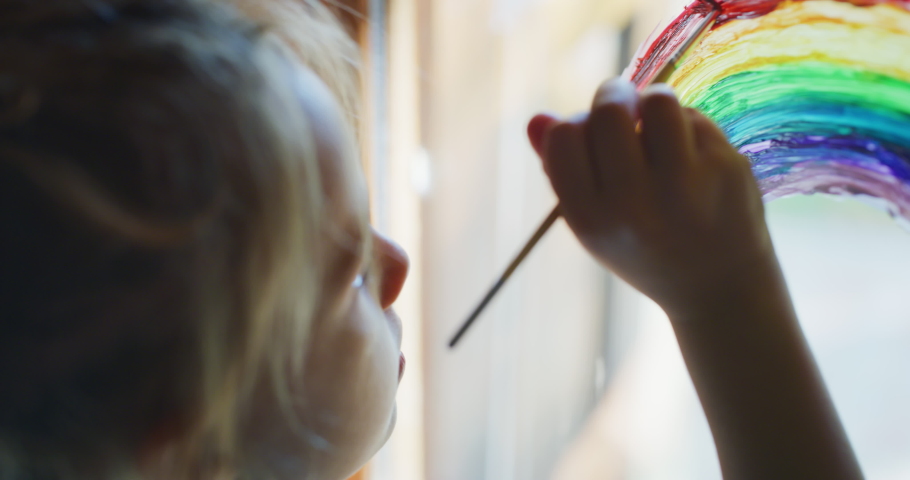 Authentic shot of a cute little creative happy smiling preschooler girl painter is drawing a rainbow on a glass of a window in a kitchen at home. Concept of happiness, arts, childhood, covid free Royalty-Free Stock Footage #1057929394
