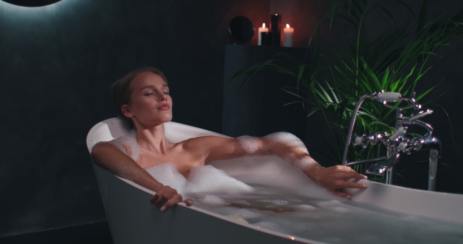 Young Woman with Beautiful Body is Lying in Bathtub with Closed Eyes Feeling Calm and Relaxed. Resting and Dreaming in Modern Luxury Bathroom. Royalty-Free Stock Footage #1057931251