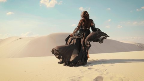 Silhouette of a happy woman running in the desert. Long black silk dress and hair flying fluttering in the wind in slow motion. A tourist is enjoying a vacation in the Dubai desert. Video footage 4K