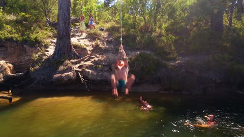 Man is diving with rope swing into the river. Cinematic dolly backwards