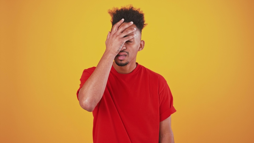Displeased young man man showing facepalm gesture, orange background