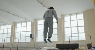 Man jumping on a trampoline to gain height before doing a forward somersault over a box in a gymnasium