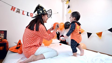 Стоковое видео: Mother with daughter in costume for celebrating Halloween at home. Mom and kid at Bedroom decoration for Trick or treat in autumn season.