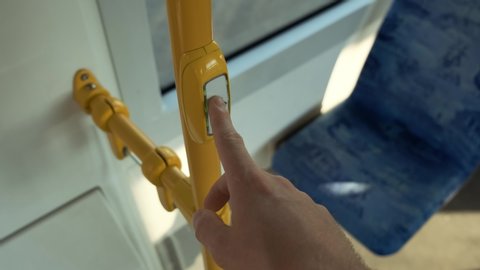 Young man presses button to open automatic door on the bus. COVID-19 public transport as Infection pathway. Stop button on a bus rail 4k