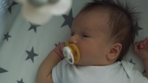 Handsome little boy sleeping sweetly in his crib. Infant sucks a pacifier and falls asleep under a baby mobile 4k