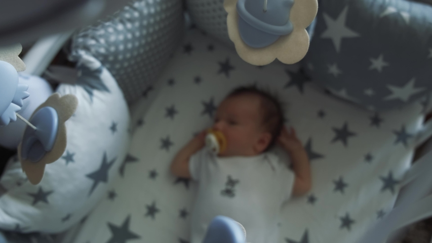 Little boy sleeping sweetly in his crib. Infant sucks a pacifier and falls asleep under a baby mobile. Defocused 4k Royalty-Free Stock Footage #1057944001