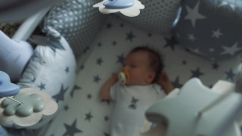 Little boy sleeping sweetly in his crib. Infant sucks a pacifier and falls asleep under a baby mobile. Defocused 4k