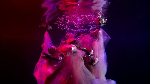 a woman with long hair spreads her hands with a translucent cloth and emerges from under it in the dark water. red and purple light. average plan