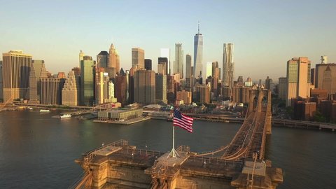 AERIAL: Flight over Brooklyn Bridge with American flag waving and East River view over Manhattan New York City Skyline in beautiful 