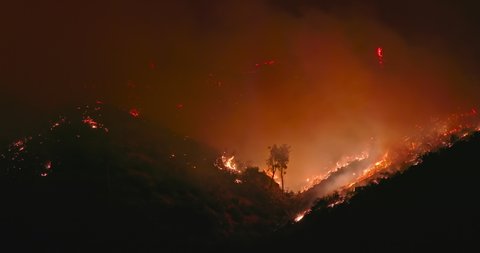 Cinematic view on wildfire in California, caused by drought and climate change, USA. Wild nature is on fire. 4k of red fire and orange smog clouds polluting the air at night. Fire emergency at night
