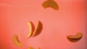 Slices of peaches fall into the water on an orange background. Up close. Slow mo - Powered by Shutterstock - Get 15% off with code: PIKWIZARD15