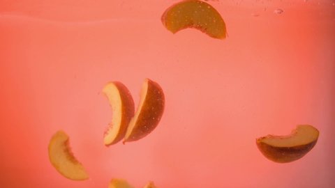Slices of peaches fall into the water on an orange background. Up close. Slow mo