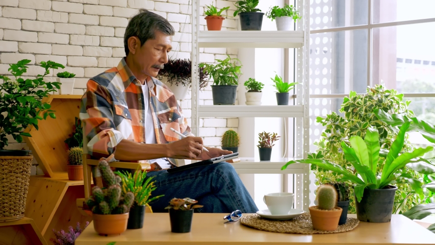 An old man sitting in a living room decorated with flower pots.