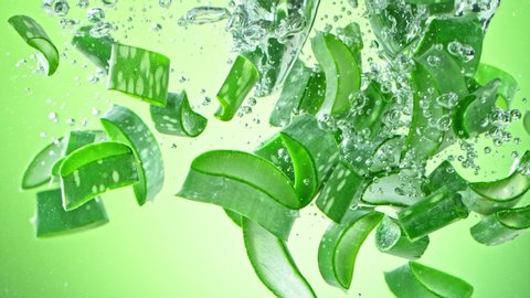 Super Slow Motion Shot of Aloe Vera Cuts Falling into Water on Green Background at 1000fps.