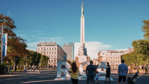 Riga, Latvia. August 5, 2020. Timelapse view of the people rushing by the monument of freedom Milda and taking photos near huge Riga sign in Riga, Latvia.