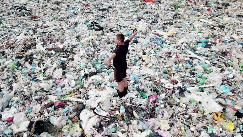 A man in a landfill photographs him from a height. The concept of environmental pollution and environmental catastrophe. | Shutterstock HD Video #1057954423