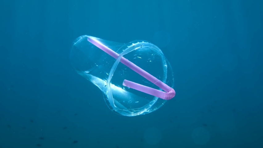 Plastic cocktail cup with a plastic straw slowly drifts underwater in blue water column in sunrays. Plastic garbage environmental pollution problem in seas and ocean. Royalty-Free Stock Footage #1057956553