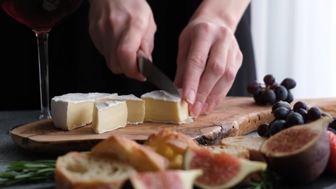 Woman slicing camembert cheese on wooden board. Gourmet appetizer or snack food. Preparation of cheese plate