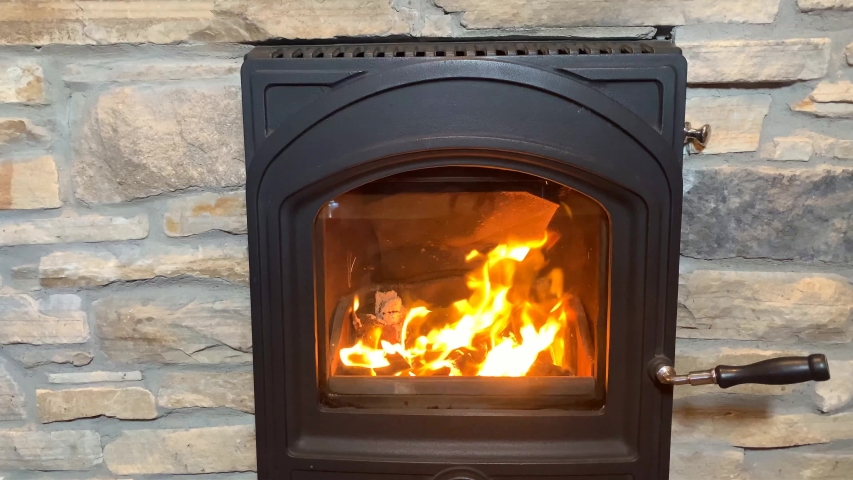 woman warms frozen hands near a bright orange fire in a black fireplace, bright flame illuminates the room, cozy home concept
