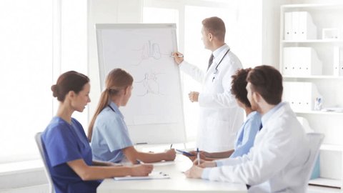 hospital, profession, medical education, people and medicine concept - group of happy doctors meeting at presentation or interns with mentor showing human organs drawings on flip board in hospital