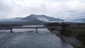 Aerial video from a drone overlooking the incredibly fresh morning landscape of Altai with mountains, the Katun River, and a concrete modern bridge across it. Altai Republic, Tyungur village, Russia.