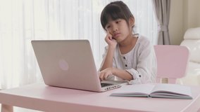 Asian homeschooling girl kid feeling bore to do homework and assigned job from remote school teacher. Child making boring face when working on computer on table. Remote online education concept.