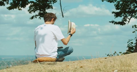 Lone guy in white t-shirt and hat reading book under tree in picnic area 