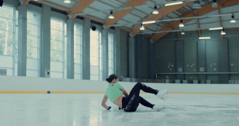 Female ice figure skater falls on ice while practicing jumps on the rink. Shot on RED cinema camera with 2x Anamorphic lens