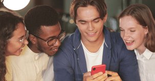 Close up view of multiethnic people looking at mobilephone screen and laughing. Young people smiling and talking while looking funny photo . Concept of friendship and positive emotions