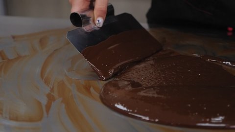 Tempering of the chocolate on the metal surface. Preparing for the production of chocolates. The pastry chef mixes the melted chocolate with a metal spatula on the table in the pastry shop.