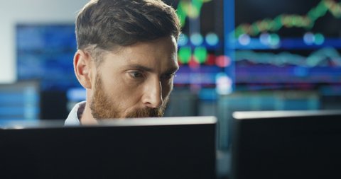 Close up of young Caucasian mman trader working at monitor computer and browsing online in trading office. Male broker following rates and bets. Manager texting at screen.