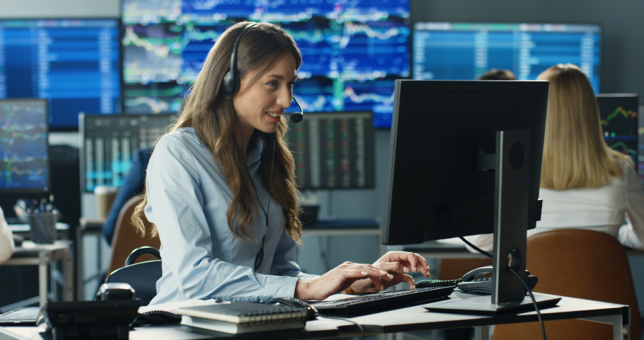 Young Caucasian pretty woman trader in headset working at monitor of computer in trading office and talking with client. Female broker typing on keyboard and speaking with customer. Sales call center. | Shutterstock HD Video #1057979566