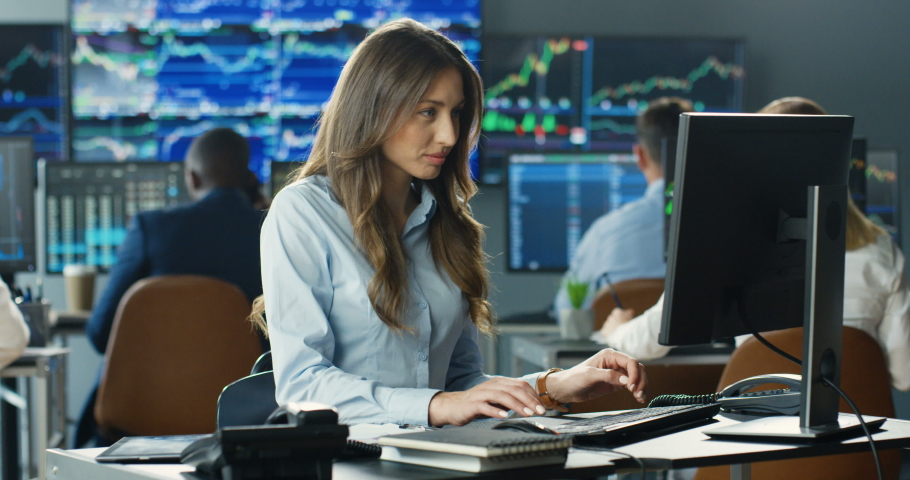 Portrait of young Caucasian beautiful woman trader working at computer, then looking at camera and smiling in trading office of exchange stock market. Female successful broker with smile on face. Royalty-Free Stock Footage #1057979569