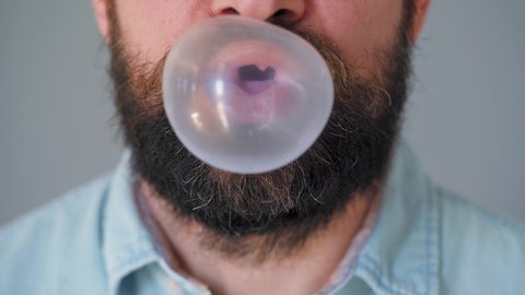 Close-up of a bearded man's mouth chewing chewing gum. Man blowing out a bubble of bubble gum