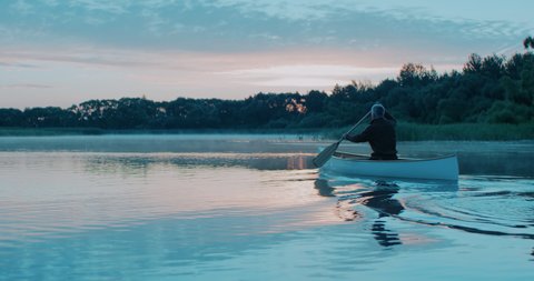 Man canoeing in a traditional wooden boat on a large lake at dawn. Shot on RED cinema camera with 2x anamorphic lens