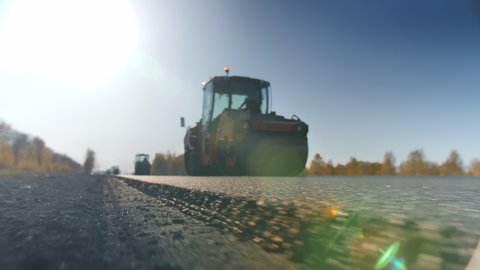 Shooting a layer of freshly laid asphalt. Road surface repair. Construction of a new road. The rollers levels and compacts the asphalt. Road rollers. Sun glare.