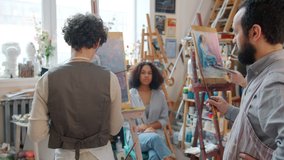 Couple of students painting portraits of cute African American girl model with help of skilled artist who is pointing at pictures talking sharing experience - Powered by Shutterstock - Get 15% off with code: PIKWIZARD15